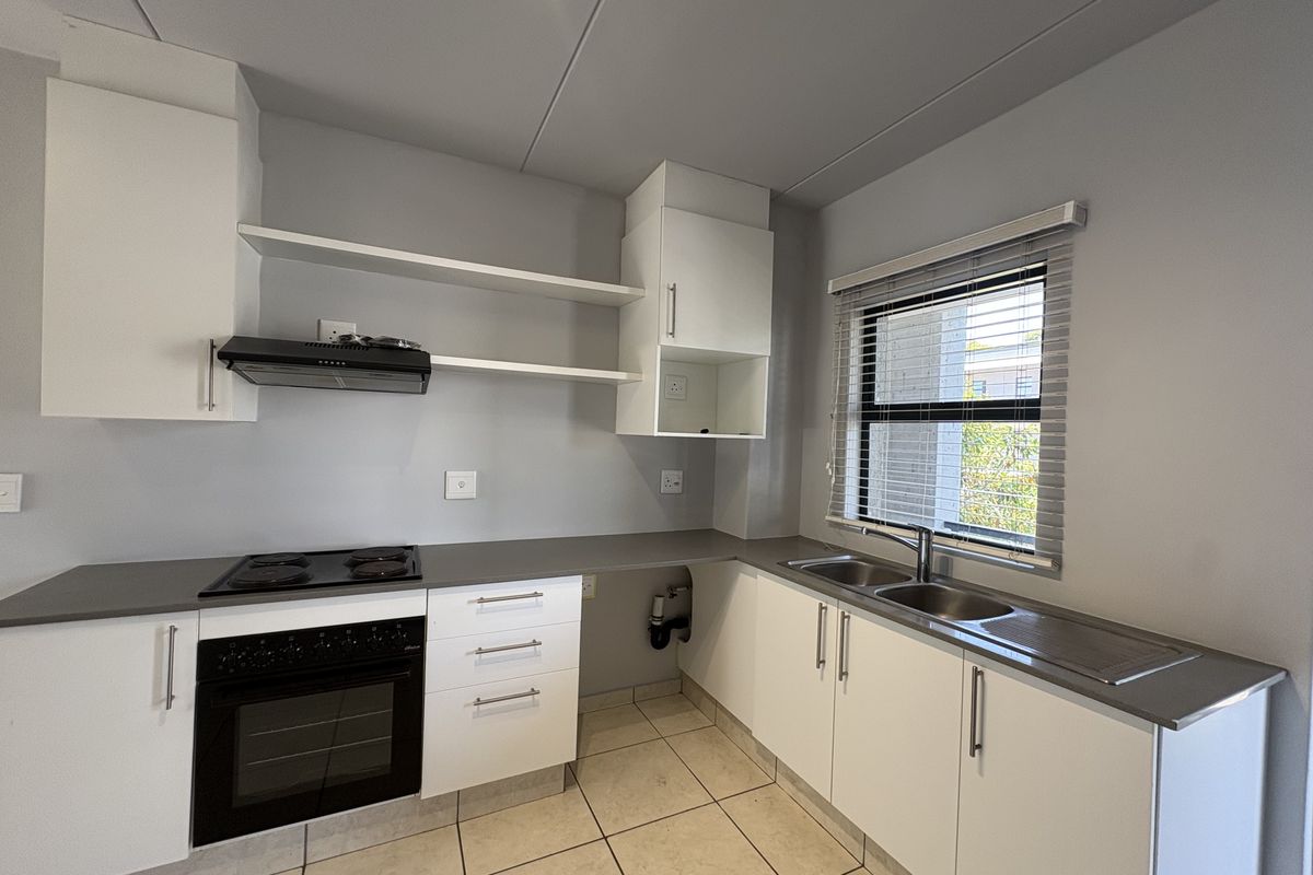 A clean, modern kitchen featuring white cabinetry, grey countertops, a built-in oven with hob, extractor fan, and a double stainless steel sink.