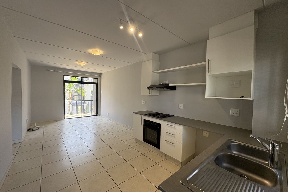 Open-plan kitchen and living area featuring tiled flooring, built-in cabinetry, integrated oven and hob, and access to a private balcony.