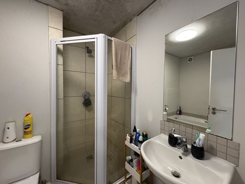 A functional bathroom featuring a shower enclosure, vanity basin, and toilet, currently showing signs of wear and ceiling staining.