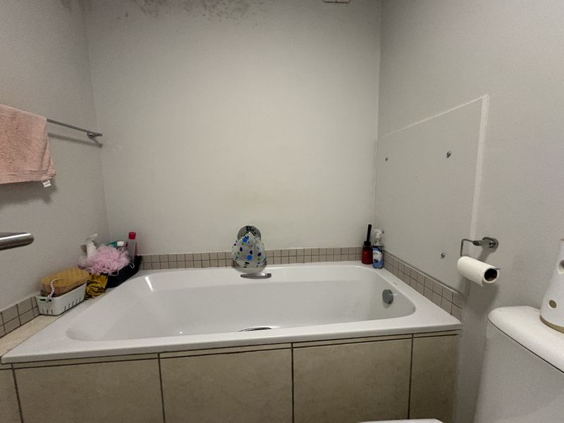 A functional bathroom featuring a built-in bathtub with tiled surround, chrome fixtures, and a towel rail. Ceiling requires maintenance due to visible staining.