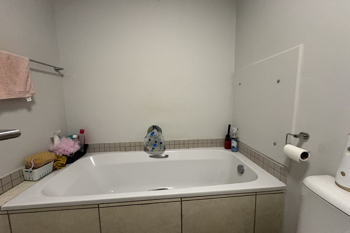 A functional bathroom featuring a built-in bathtub with tiled surround, chrome fixtures, and a towel rail. Ceiling requires maintenance due to visible staining.