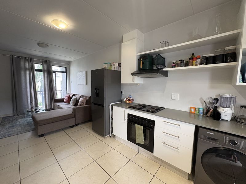 Open-plan living area featuring a modern kitchen with built-in appliances, tiled flooring, and direct access to a balcony through sliding glass doors.