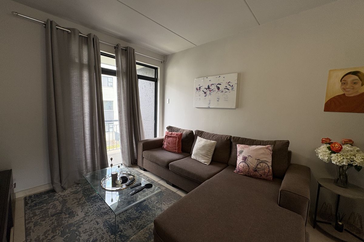 A well-lit living room featuring neutral tiled flooring and a sliding glass door providing access to an outdoor area.