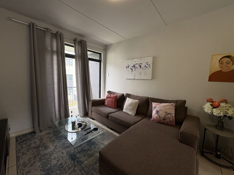 A well-lit living room featuring neutral tiled flooring and a sliding glass door providing access to an outdoor area.