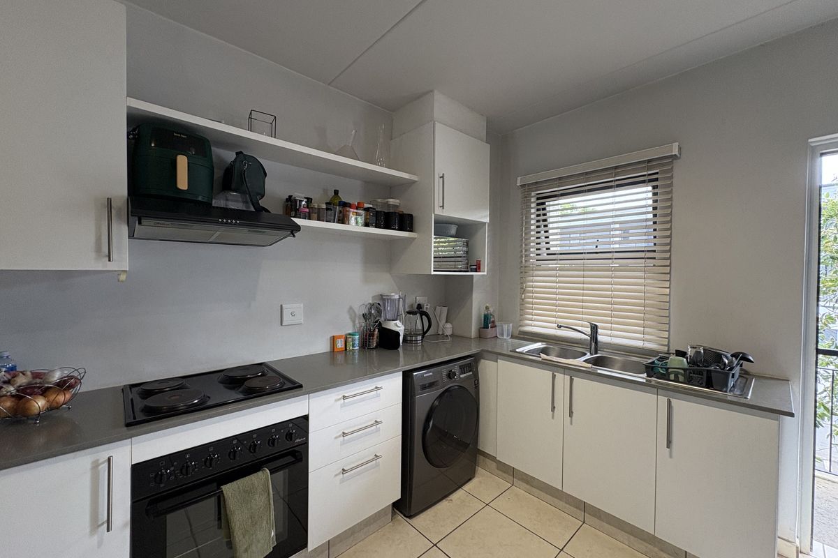 Modern kitchen featuring white cabinetry, stone-look countertops, integrated electric oven and hob, double sink, and tiled flooring with natural light.