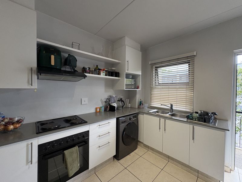 Modern kitchen featuring white cabinetry, stone-look countertops, integrated electric oven and hob, double sink, and tiled flooring with natural light.