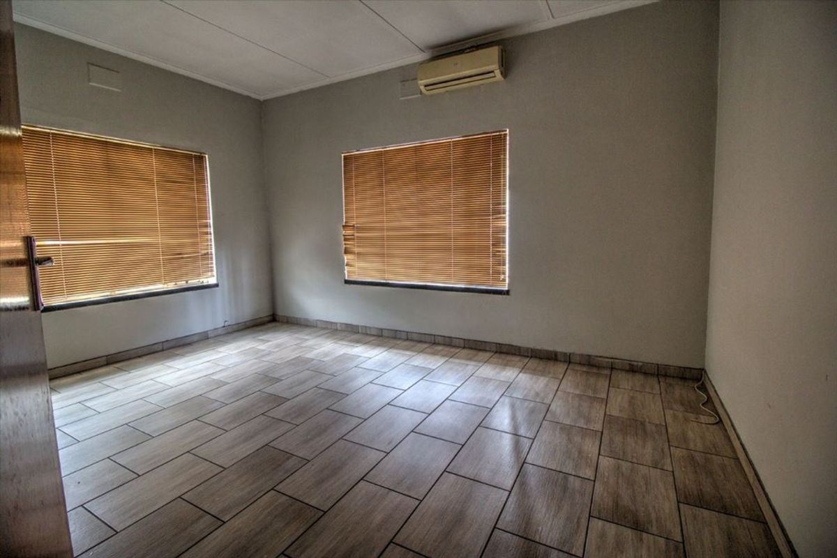 An empty bedroom featuring wood-look tiled flooring, neutral walls, and a wall-mounted split-system air conditioning unit.