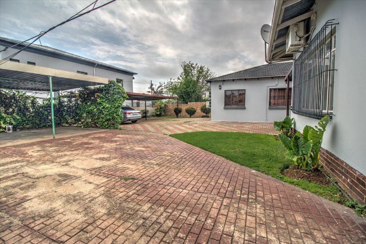 Rear exterior view featuring a paved driveway, carport, and security bars on windows, providing functional outdoor space and parking.