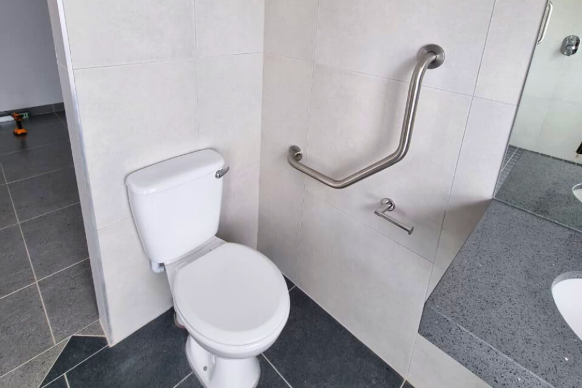 A functional bathroom featuring a toilet, a wall-mounted grab rail for accessibility, and a vanity with a stone countertop.