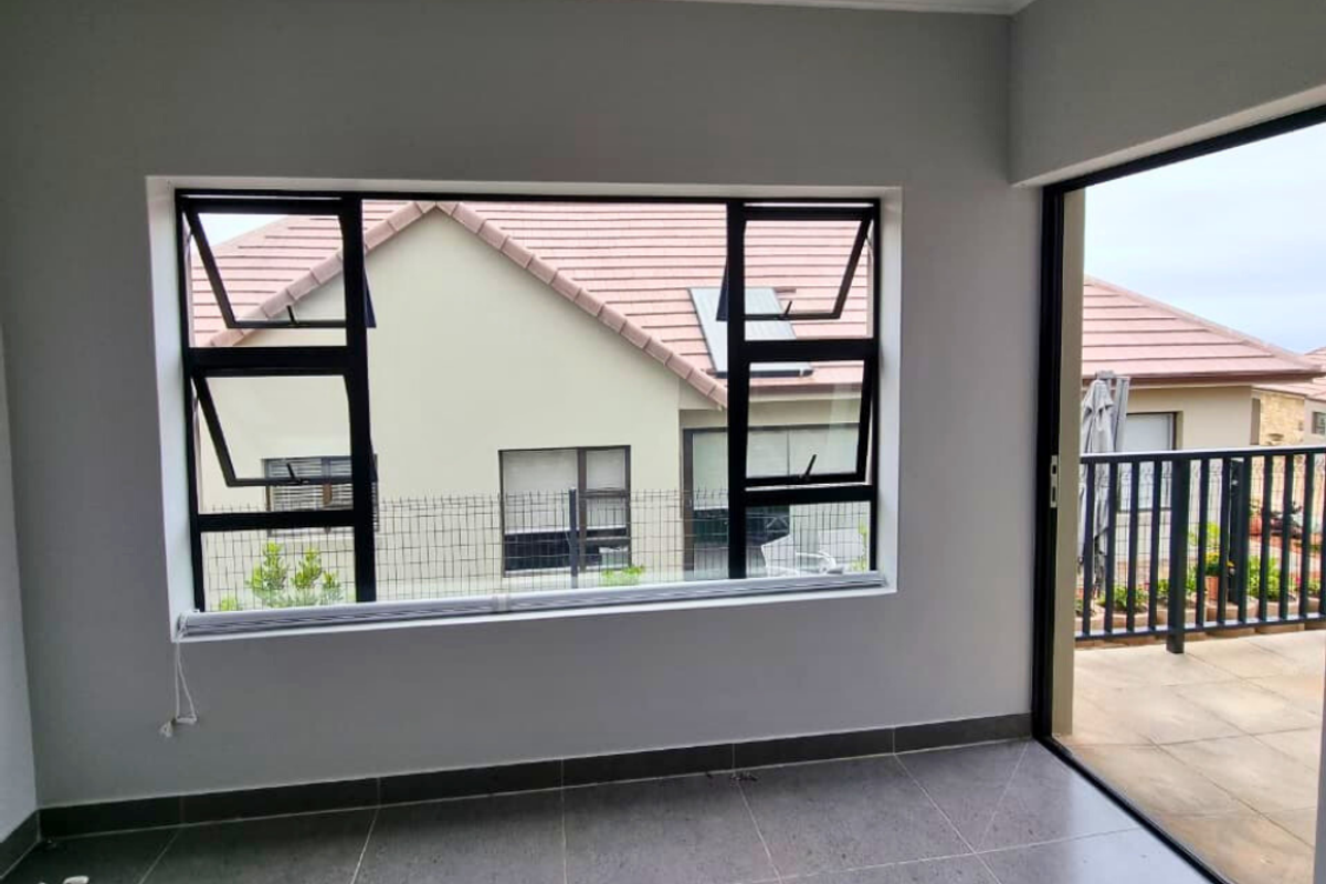 A bright, modern interior space featuring large black-framed windows and a sliding door leading to an outdoor patio area with tiled flooring.