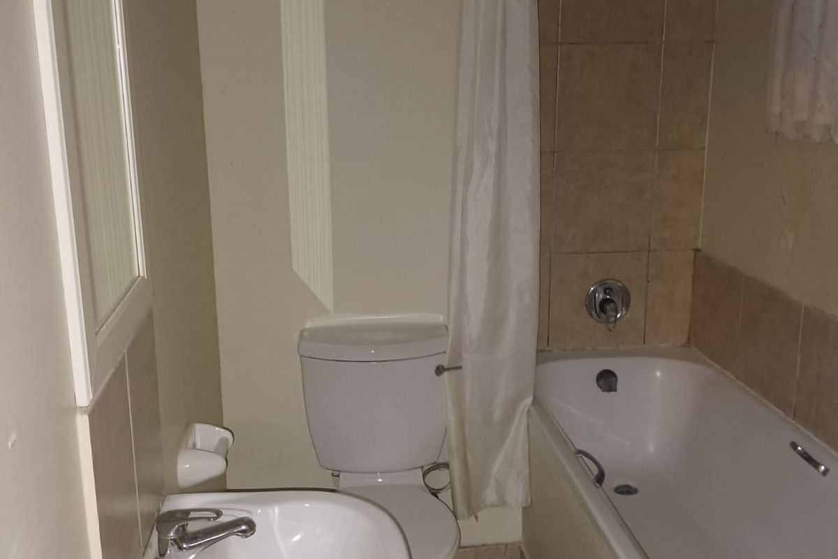 A functional bathroom featuring a pedestal basin, a standard toilet, and a shower-over-bath combination with tiled splashbacks.