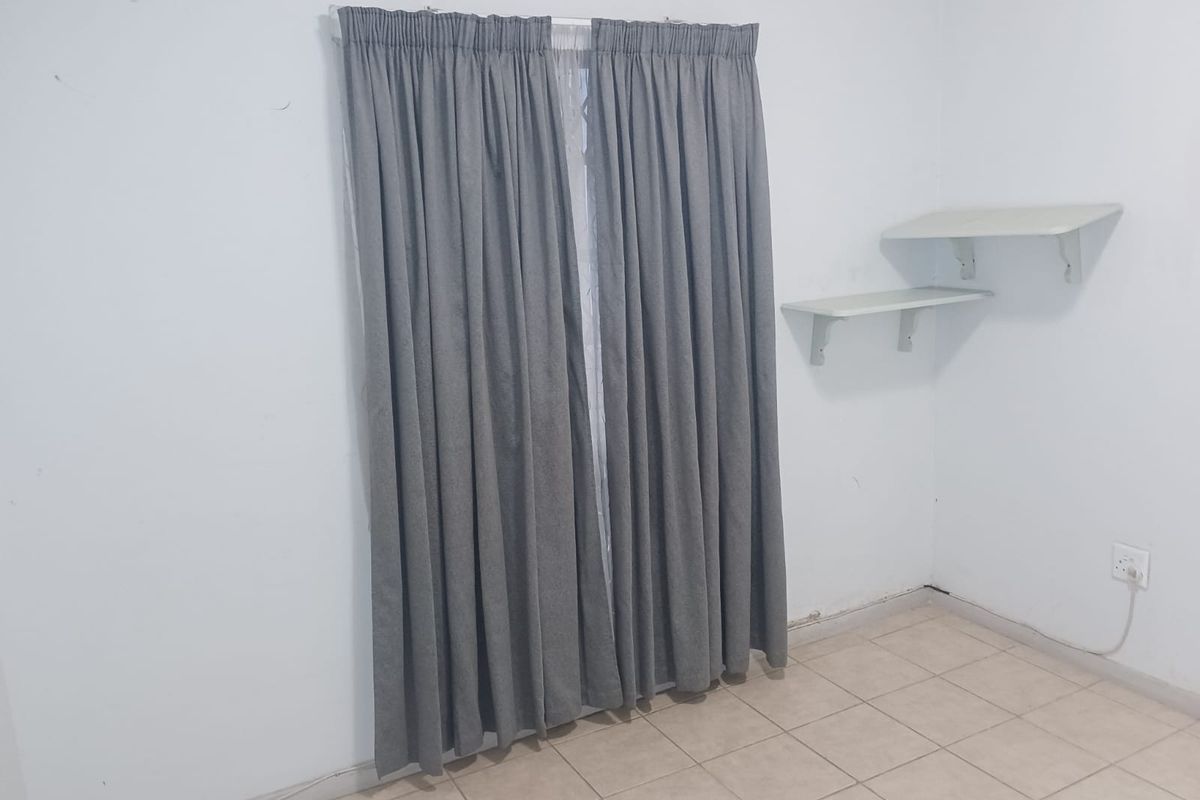 A simple bedroom featuring tiled flooring, wall-mounted shelving, and grey curtains covering the window.