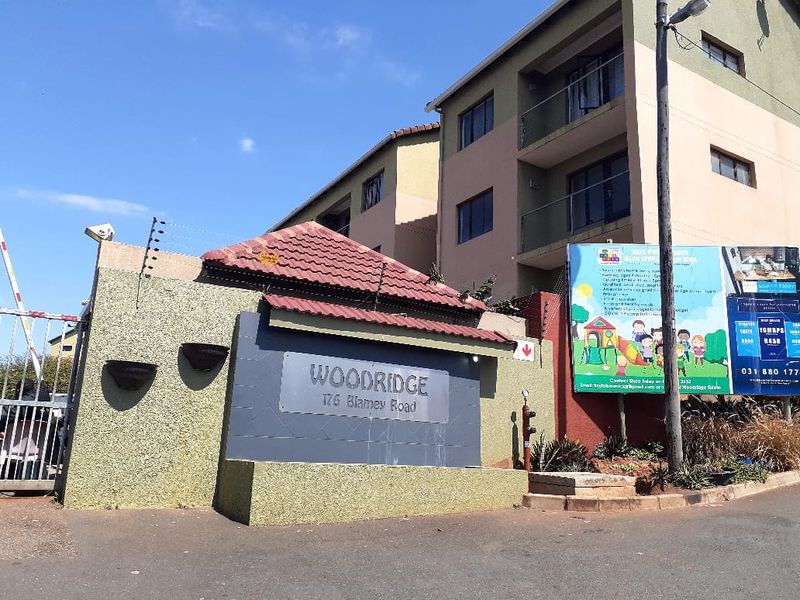 Exterior view of the Woodridge apartment complex entrance, featuring a gated access point, signage, and multi-story residential building facade.