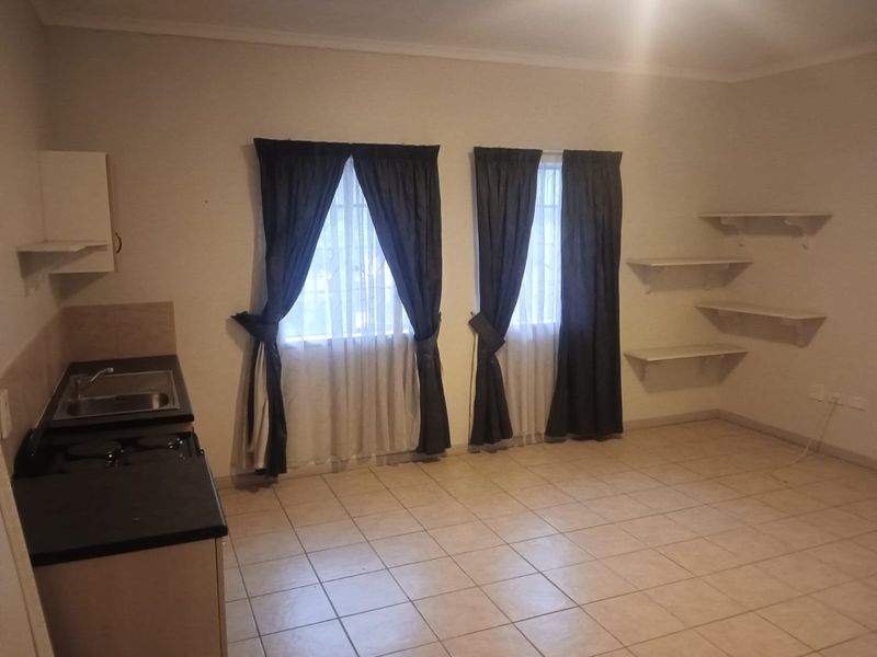 An open-plan living and kitchen area featuring tiled flooring, built-in kitchen cabinetry with a sink, and wall-mounted shelving units.