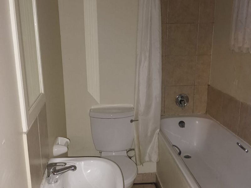 A functional bathroom featuring a pedestal basin, a standard toilet, and a shower-over-bath combination with tiled splashbacks.