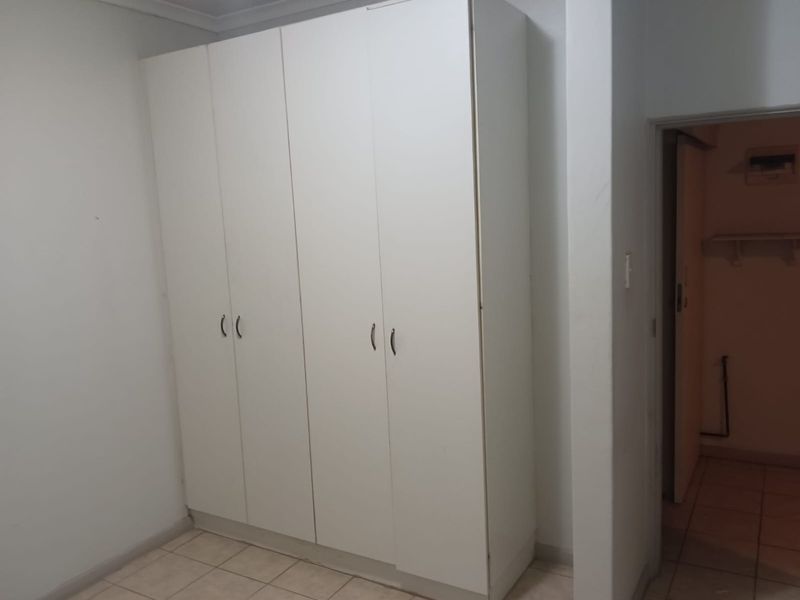 A bedroom featuring built-in white cabinetry and tiled flooring, with an adjacent doorway leading to a secondary utility or storage space.