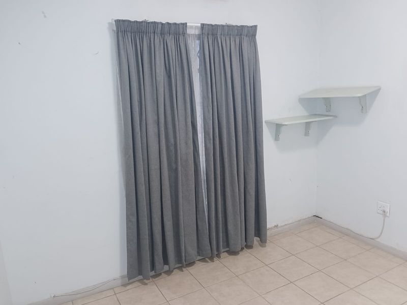 A simple bedroom featuring tiled flooring, wall-mounted shelving, and grey curtains covering the window.