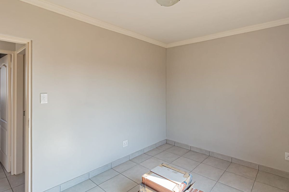 A neutral-toned bedroom featuring tiled flooring, crown molding, and an adjoining bathroom entrance.