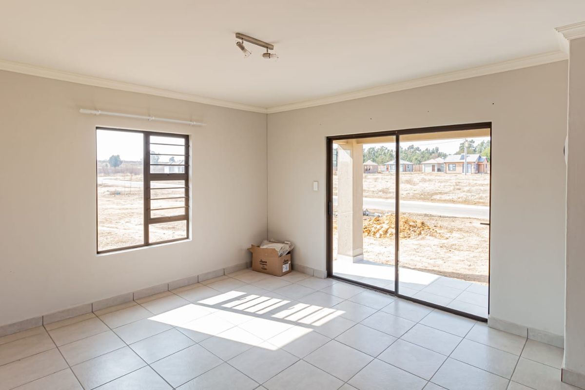 A bright, open-plan living area featuring tiled flooring, a sliding glass door leading to the patio, and large windows providing natural light.