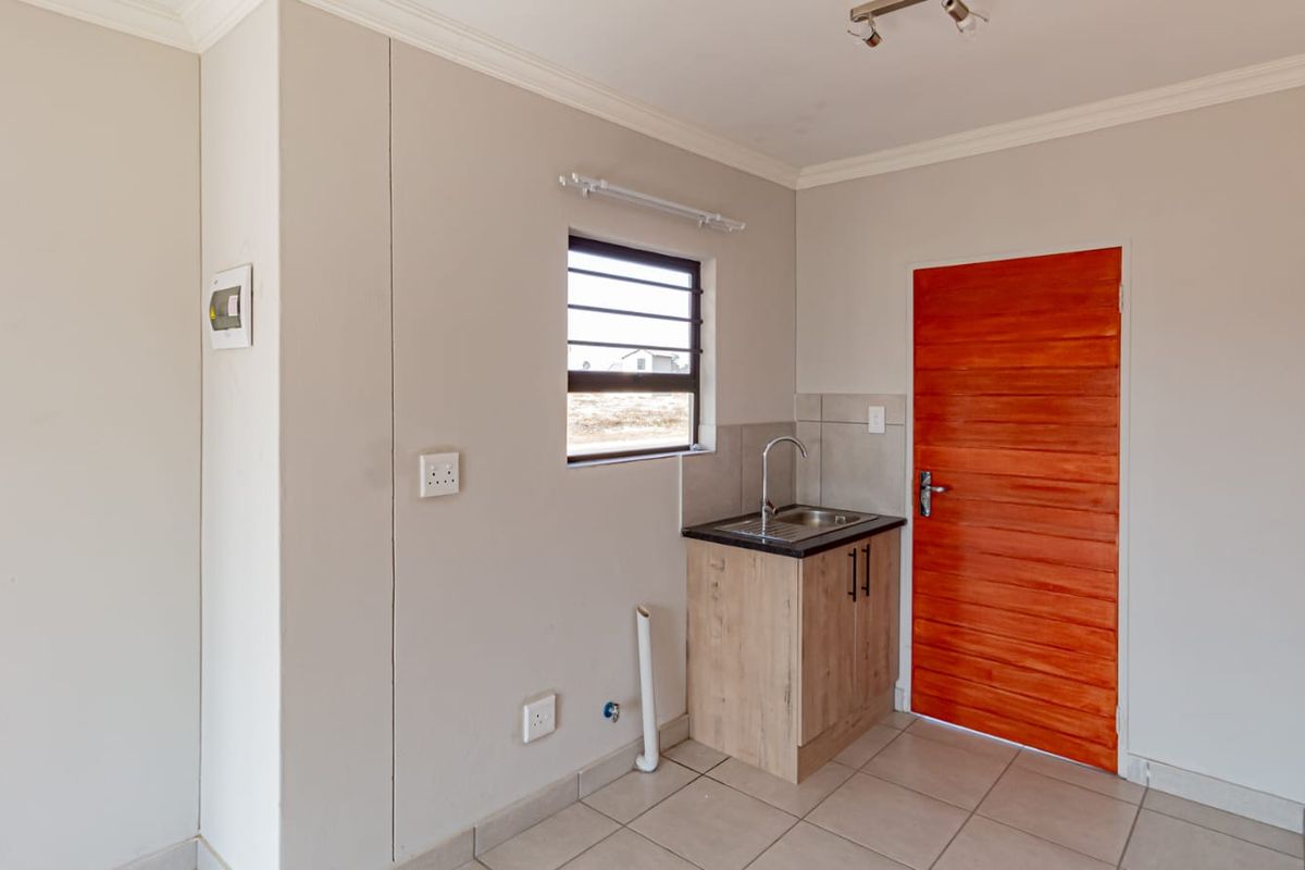 A compact kitchenette area featuring a single sink unit, tiled flooring, and a solid timber door, providing a functional utility space.