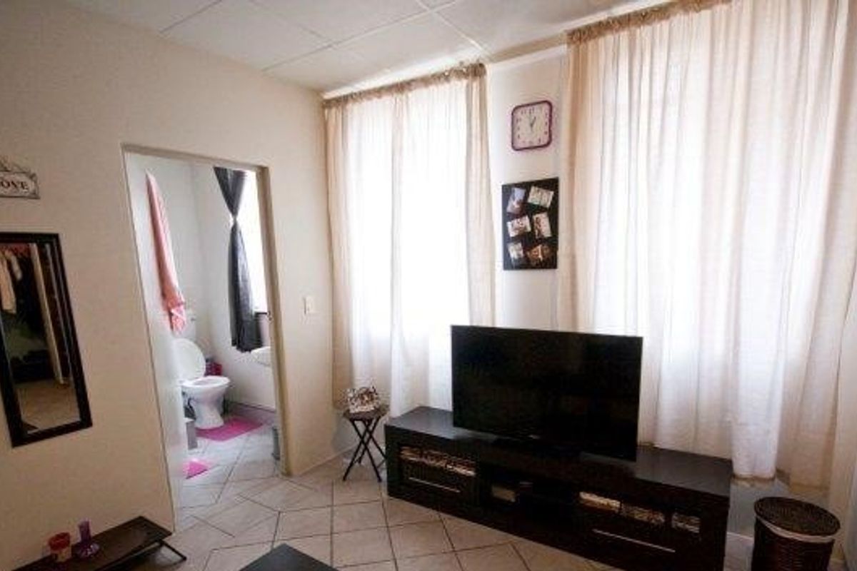 A living room area featuring tiled flooring and large windows with curtains, providing access to an adjacent bathroom.