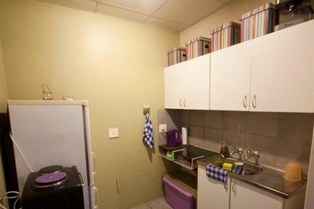 A compact scullery area featuring wall-mounted cabinetry, a stainless steel sink, and tiled splashback, providing essential utility space.