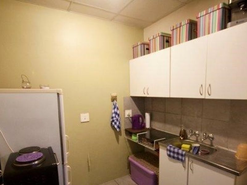 A compact scullery area featuring wall-mounted cabinetry, a stainless steel sink, and tiled splashback, providing essential utility space.