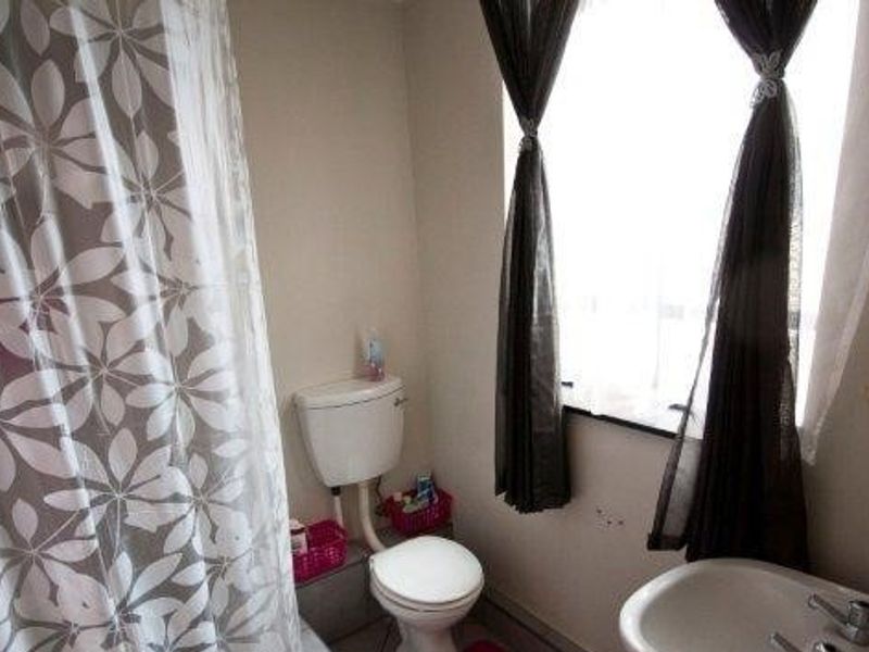 A functional bathroom featuring a standard toilet, pedestal basin, and a shower area with a curtain enclosure.