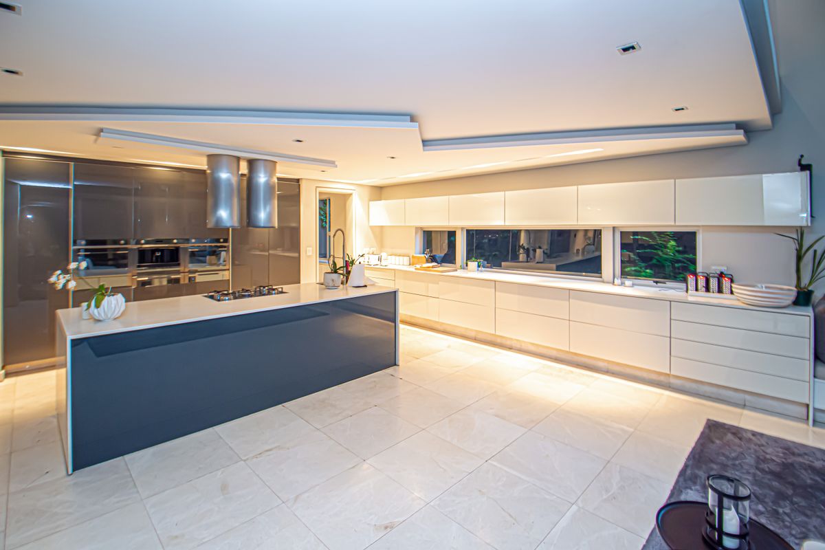 Modern, high-end kitchen featuring sleek handleless cabinetry, a large central island with a built-in cooktop, dual extractor fans, and polished stone flooring.
