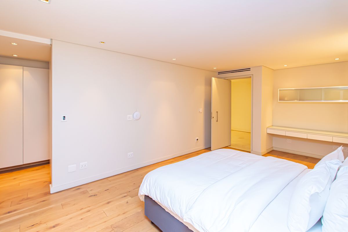 Spacious bedroom featuring light timber flooring, built-in cabinetry, recessed ceiling lighting, and a sleek integrated wall-mounted desk unit.
