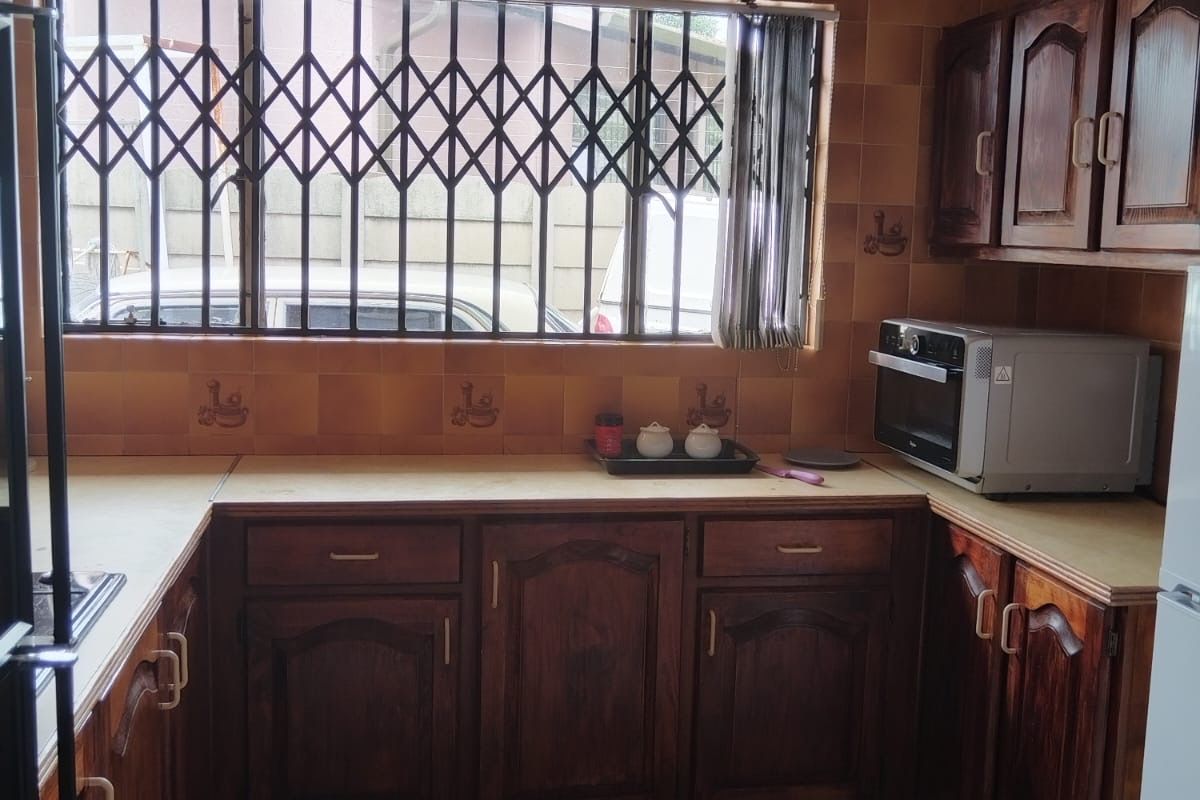 A functional kitchen featuring dark wood cabinetry, tiled countertops, and a window fitted with security bars.
