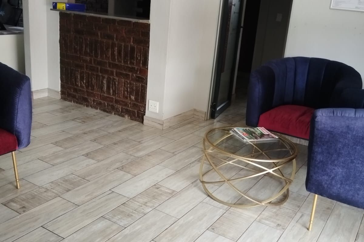 A bright living area featuring wood-look ceramic floor tiles and a distinctive exposed brick feature wall with a service counter opening.