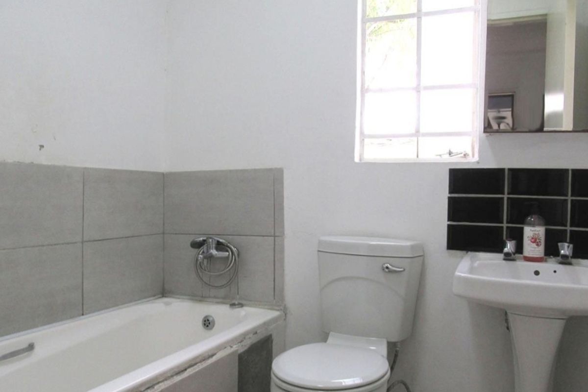 A functional bathroom featuring a standard bathtub, pedestal basin, and toilet, with a window providing natural light.