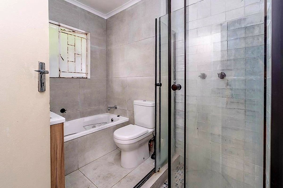 A functional bathroom featuring a built-in bathtub, a separate glass-enclosed shower, and a modern toilet with neutral wall and floor tiling.