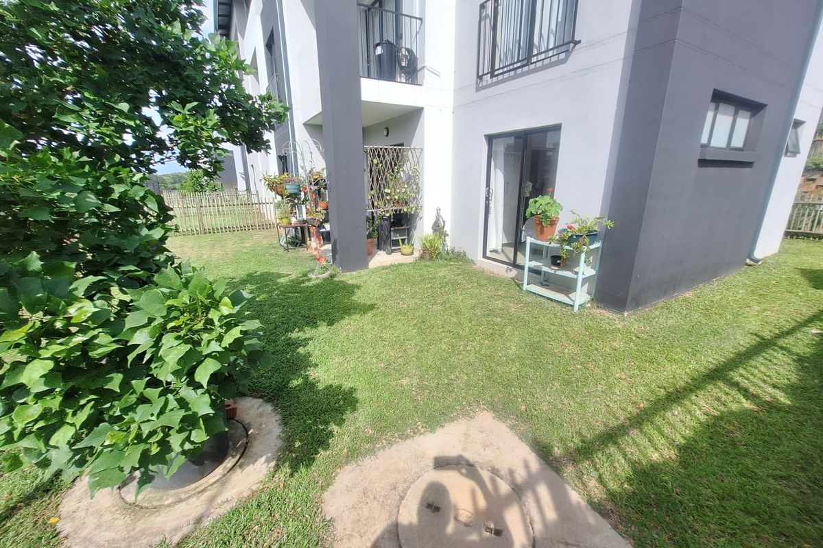 A private ground floor garden area featuring a small lawn, concrete inspection cover, and direct access to the apartment via sliding glass doors.