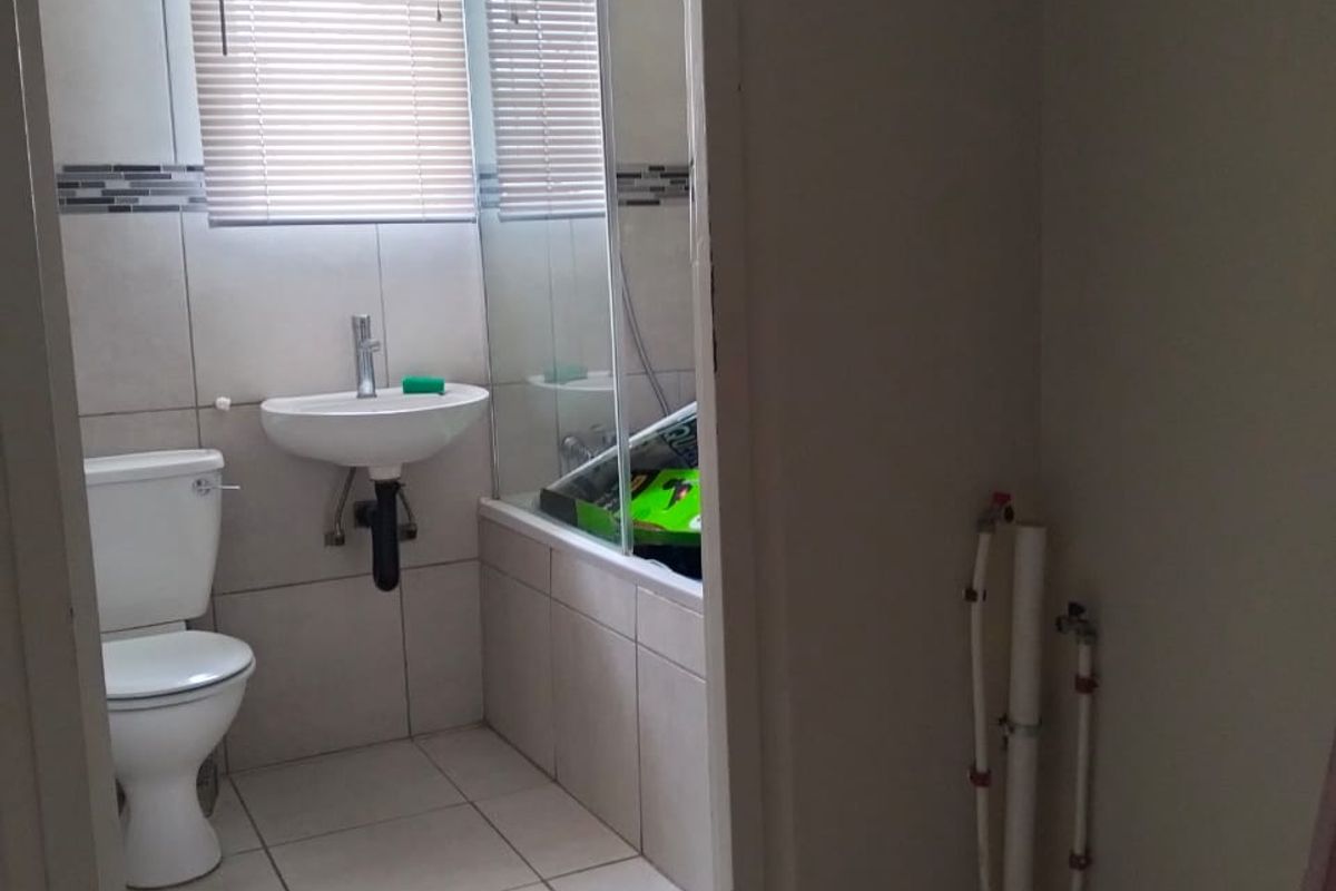 A functional bathroom featuring a wall-mounted basin, toilet, and a shower-over-bath combination with tiled finishes and a window blind.
