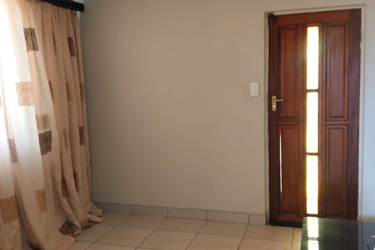 A functional living area featuring tiled flooring, a wooden entrance door with glass inserts, and neutral wall finishes.