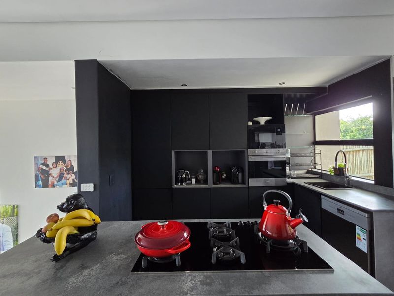Modern kitchen featuring matte black cabinetry, stone countertops, a central island with a gas hob, and integrated appliances.