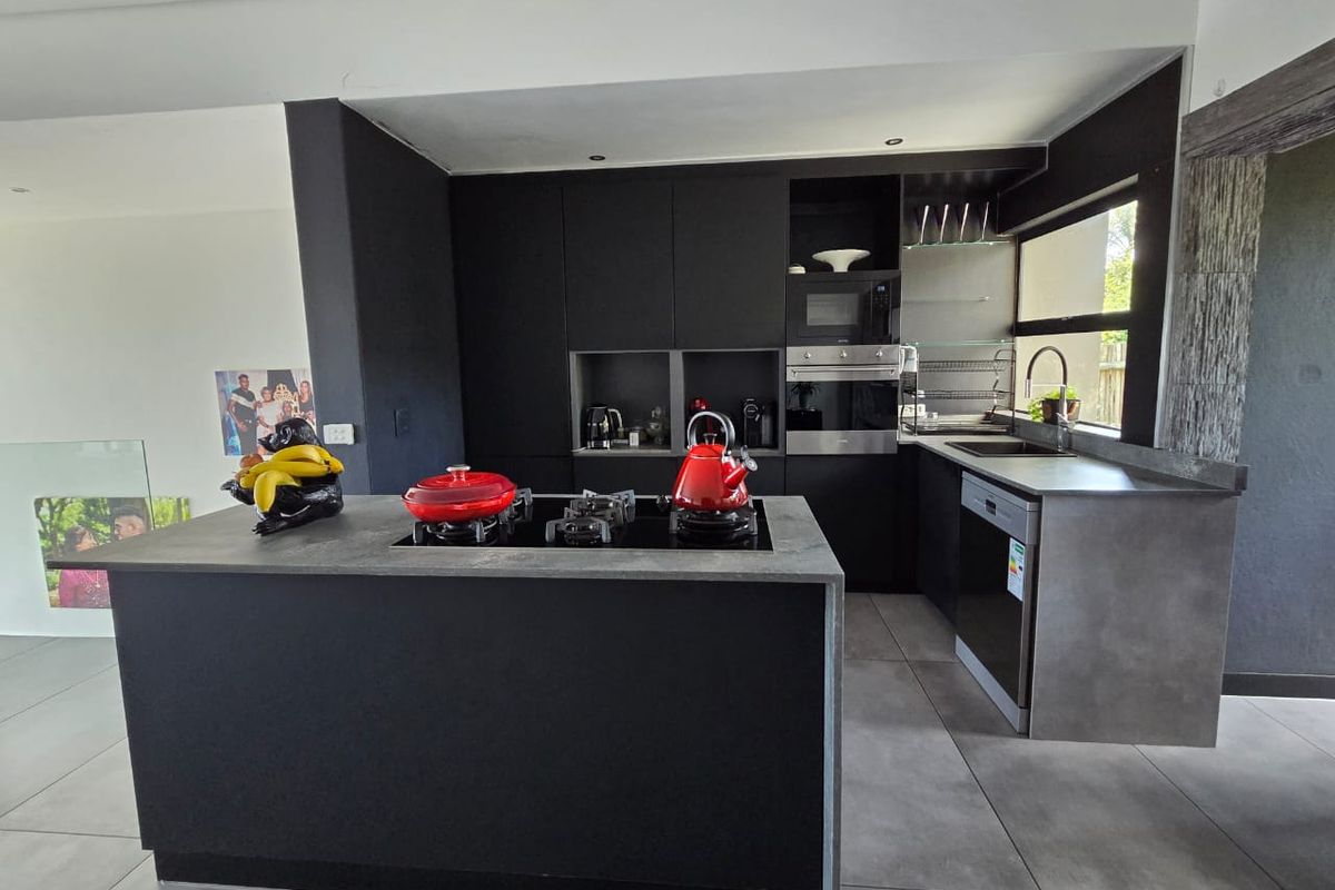 Modern kitchen featuring sleek black cabinetry, a central island with a gas hob, stone countertops, and integrated appliances.