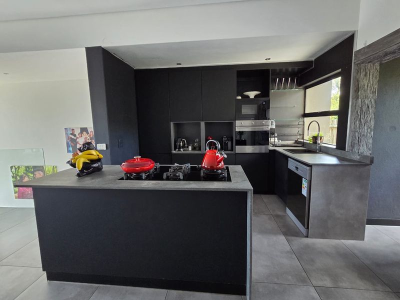 Modern kitchen featuring sleek black cabinetry, a central island with a gas hob, stone countertops, and integrated appliances.