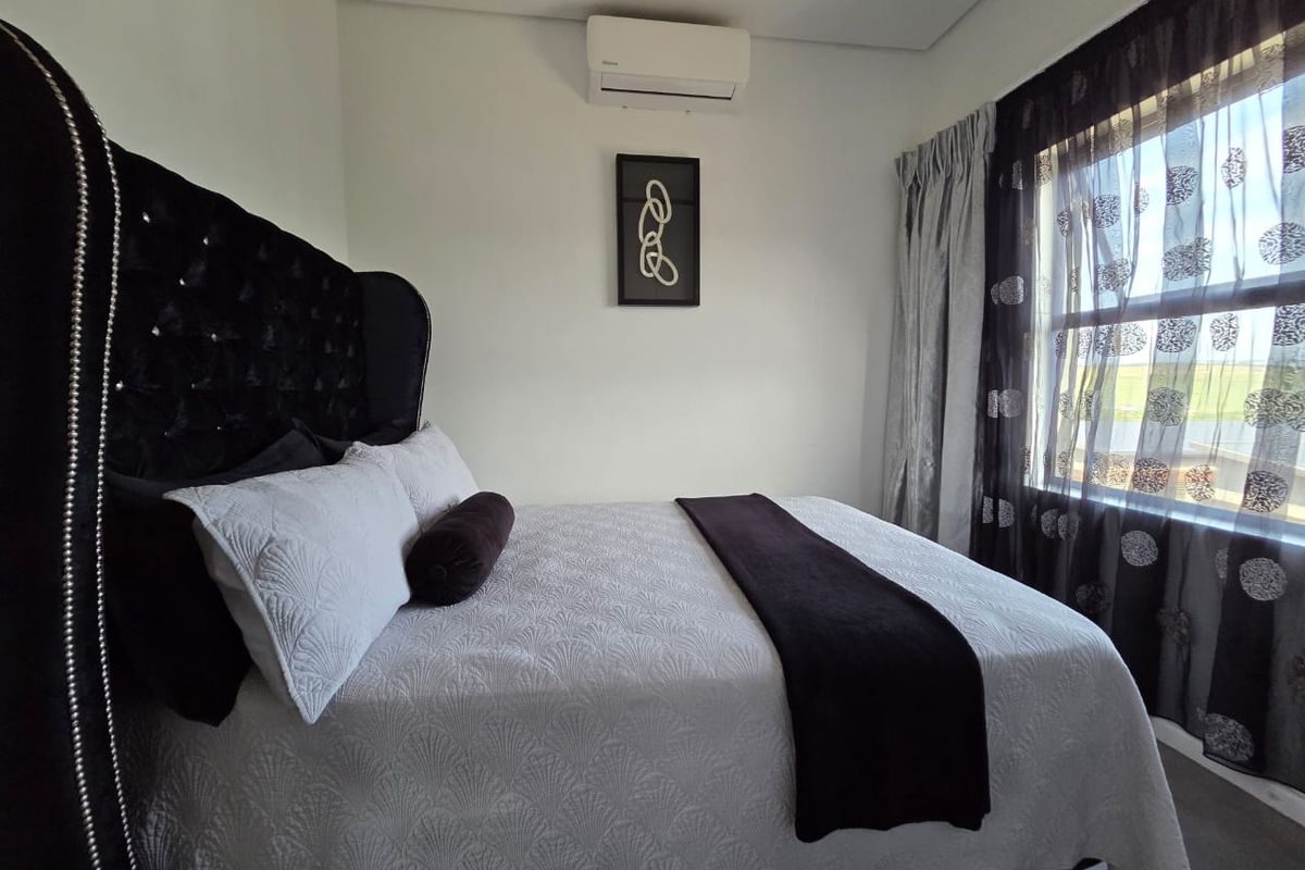 A well-maintained bedroom featuring a wall-mounted split-system air conditioner and large window with installed curtain tracks.