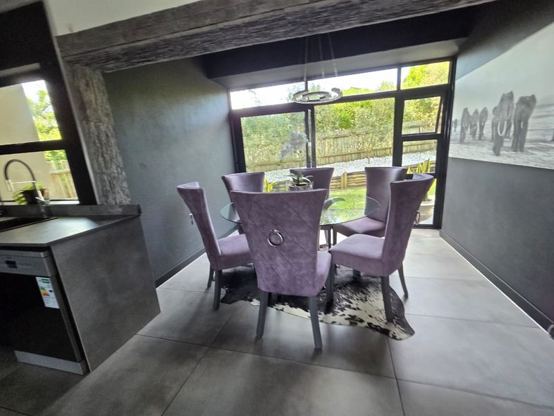 Modern open-plan dining area featuring large format floor tiles, exposed timber beam detail, and expansive black-framed sliding doors opening to the garden.