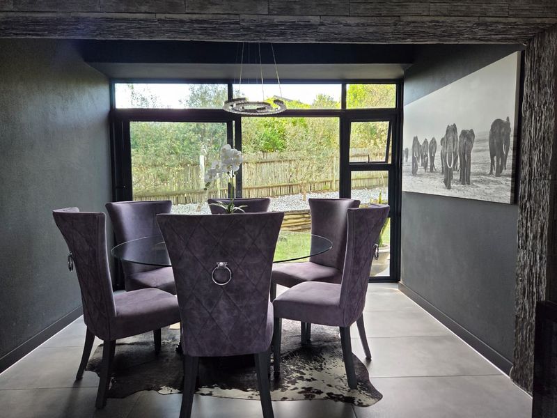 Modern dining area featuring large format floor tiles, dark feature walls, and expansive black aluminium framed windows overlooking the garden.