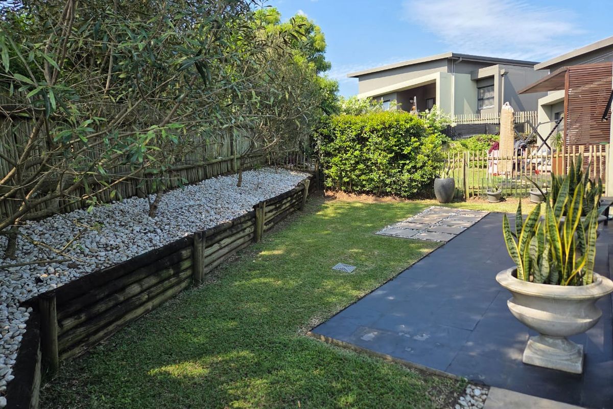 A well-maintained rear garden featuring a paved patio, a manicured lawn, and a tiered timber retaining wall with decorative stone landscaping.