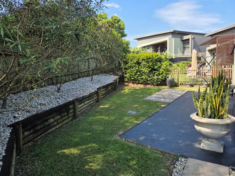 A well-maintained rear garden featuring a paved patio, a manicured lawn, and a tiered timber retaining wall with decorative stone landscaping.