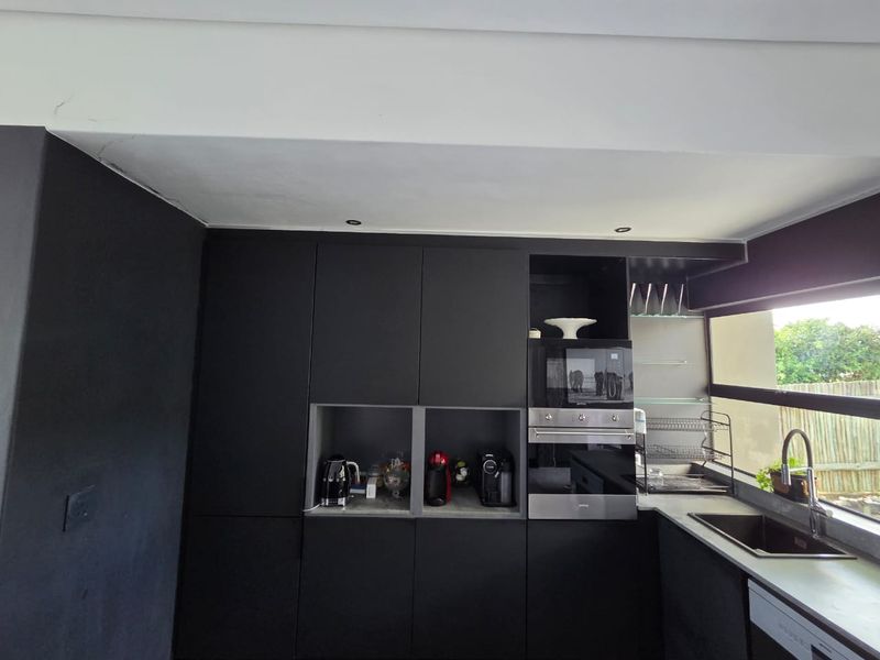 Modern kitchen featuring matte black cabinetry, integrated oven and microwave, undermount sink with mixer tap, and recessed ceiling lighting.