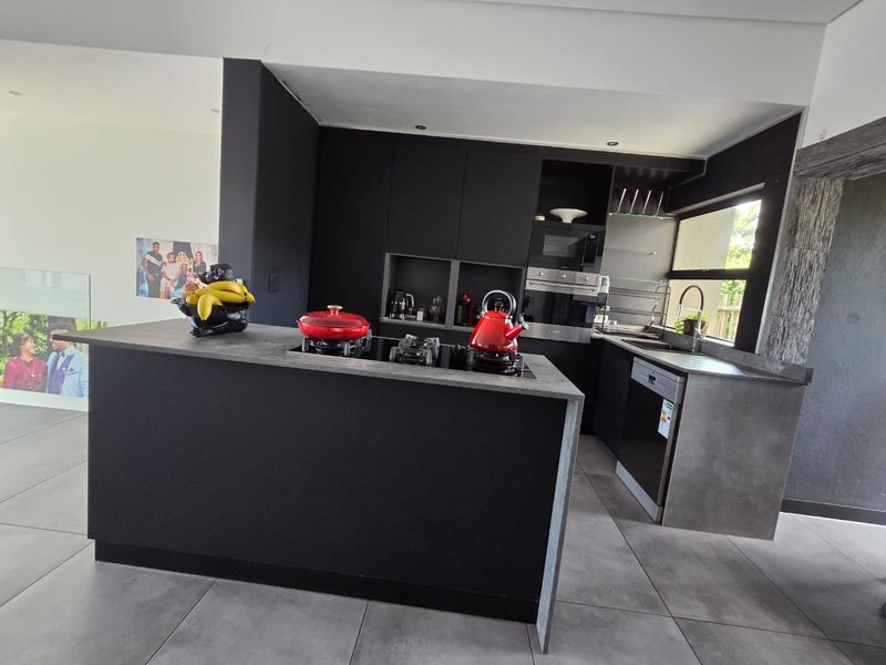 Modern kitchen featuring matte black cabinetry, a central island with a built-in hob, integrated appliances, and sleek tiled flooring.