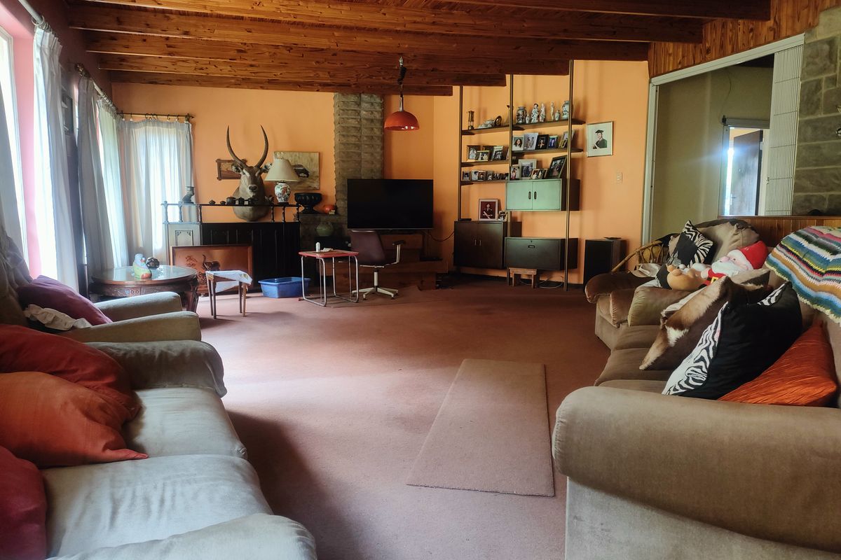 Spacious living room featuring exposed timber beam ceilings, a brick fireplace surround, and carpeted flooring.