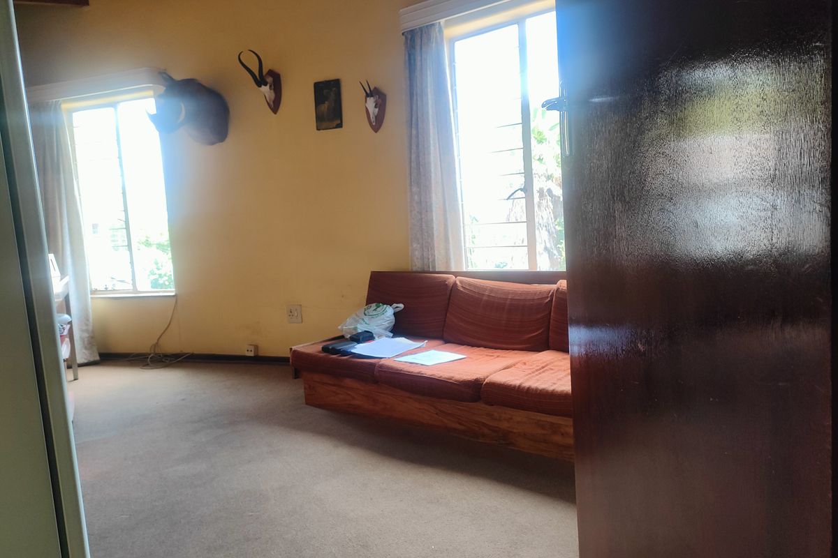 A bedroom featuring carpeted flooring, large windows allowing natural light, and exposed wooden ceiling beams.