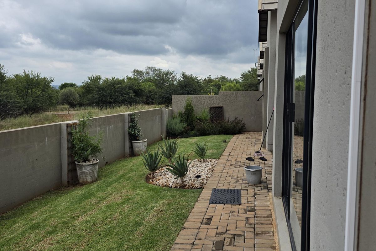 A private rear garden featuring a paved walkway, manicured lawn, and perimeter boundary wall, providing a clean outdoor space.